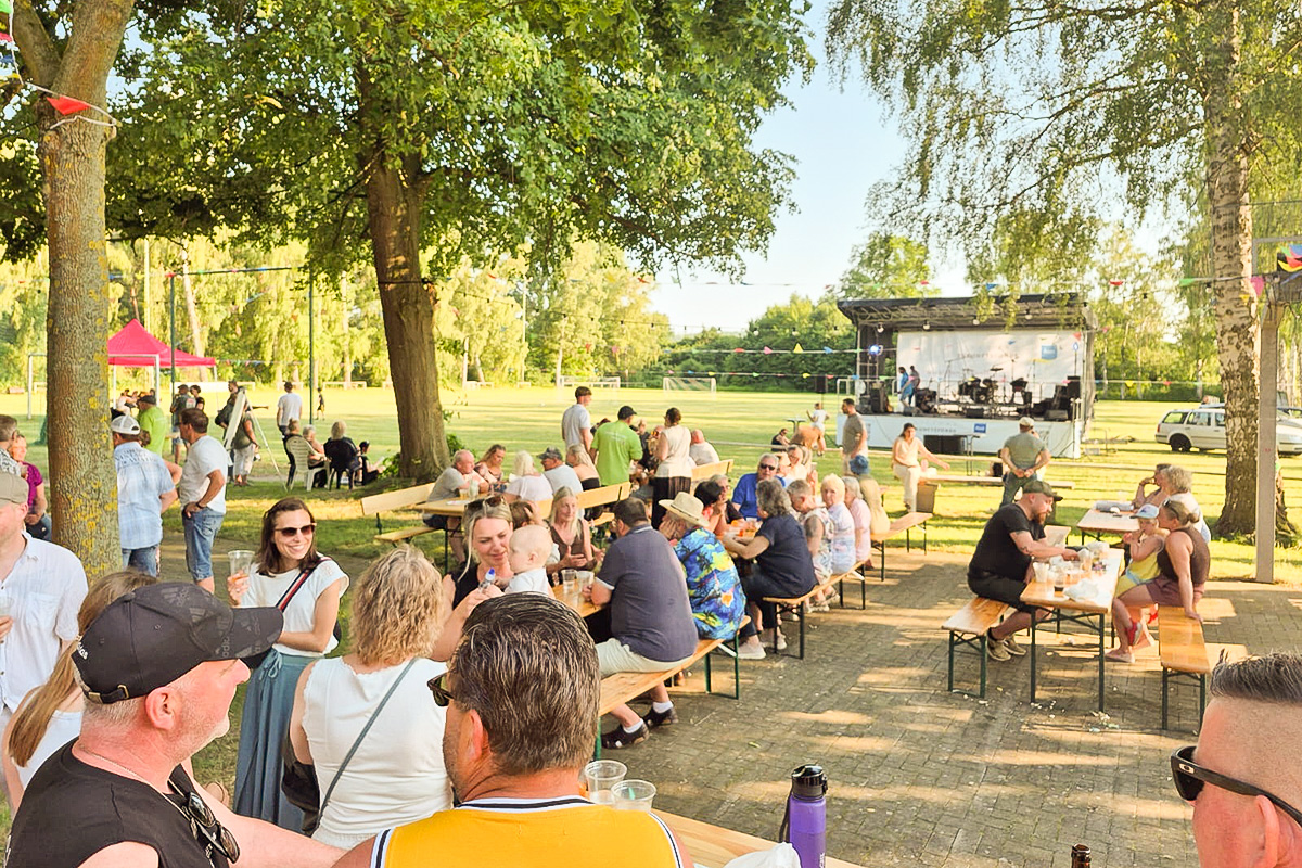 Der gut gefüllte Sportplatz mit der Bühne im Hintergrund. Bei hohen Temperaturen spendete der alte Baumbestand ein wenig Schatten.