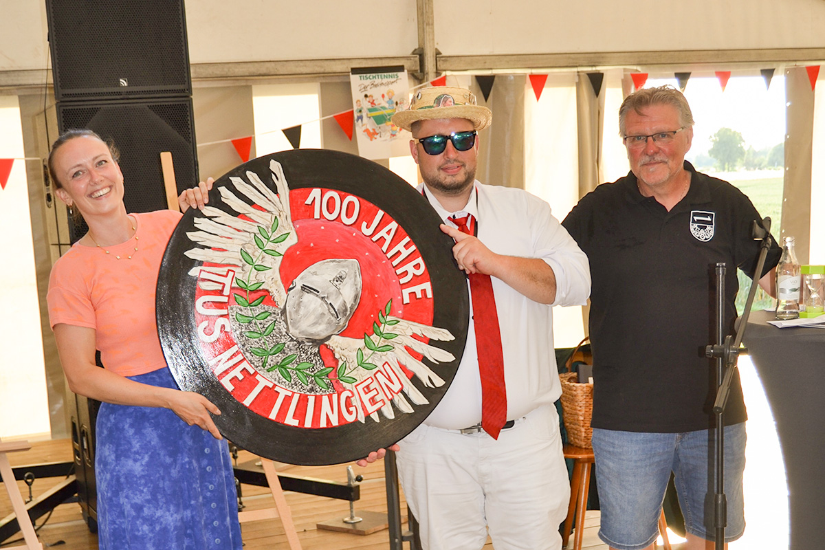 Die einmalige Ehrenscheibe zum 100-jährigen Vereinsjubiläum geht an Marcel Bodenburg (Mitte). Gestaltet wurde das Unikat von der Nettlinger Künstlerin Lisa Elias (links). Rechts gratuliert der 1. Vorsitzende Andreas Bähre.